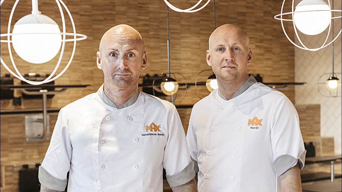 Två män med max-kläder med titlarna Vice VD och Verställande Direktör. I MAX-restaurangmiljö. Foto.