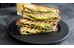 Grillad sandwich med avokado och pesto på svart tallrik. Foto.