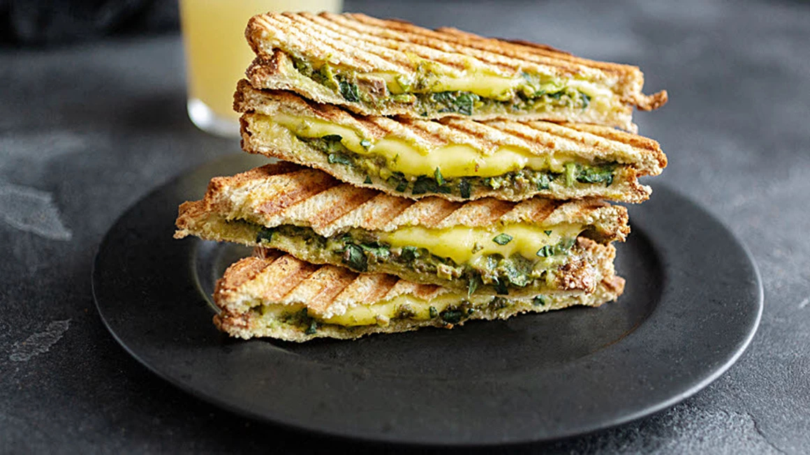 Grillad sandwich med avokado och pesto på svart tallrik. Foto.