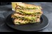 Grillad sandwich med avokado och pesto på svart tallrik. Foto.