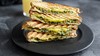 Grillad sandwich med avokado och pesto på svart tallrik. Foto.