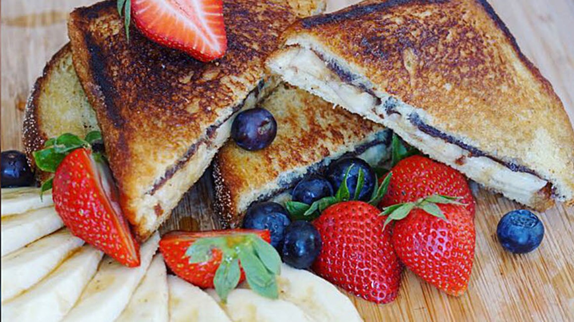 Toastsmörgås med nutella, skivad banan och färska blåbär och jordgubbar. Skuren i trekanter. Foto