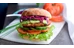 Vegetarisk hamburgare med halloumi, gurkskivor, tomatskivor och svamp på skärbräda. Foto.