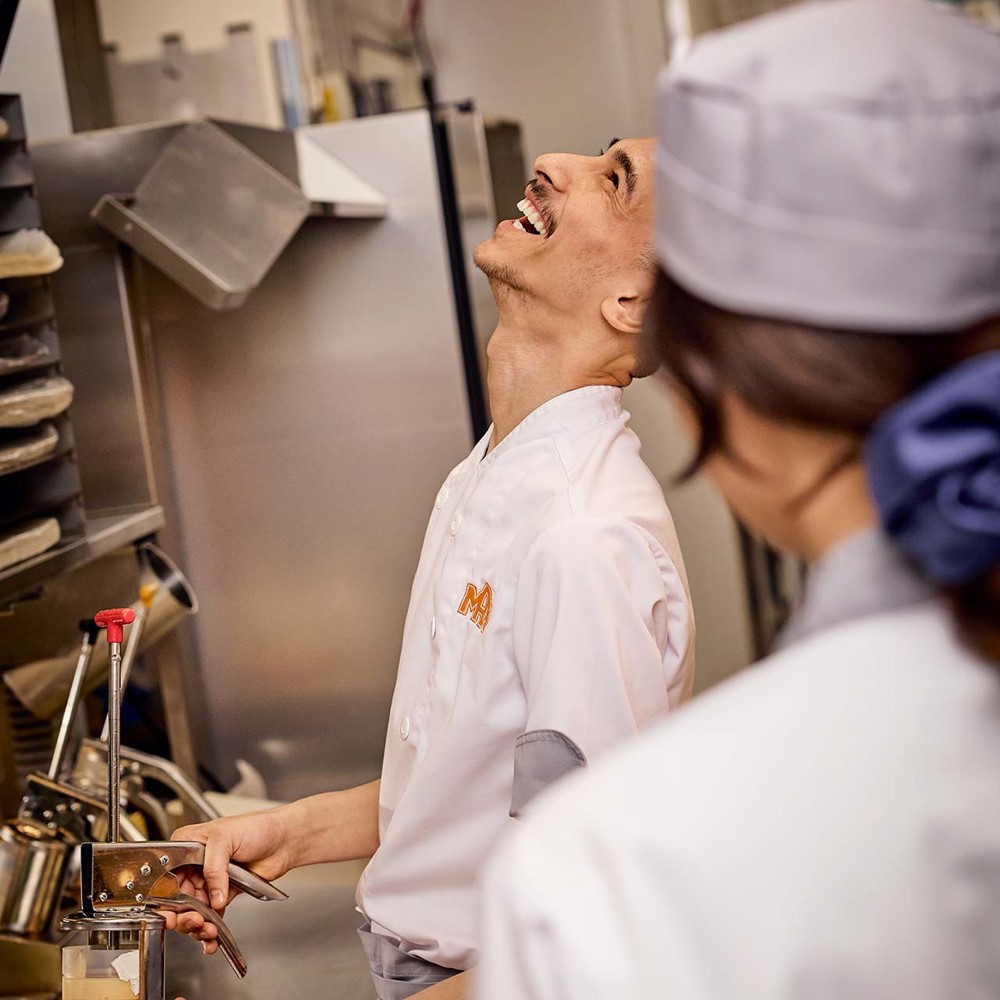 <p>Restaurangpersonal står vid en av stationerna i köket och skrattar.</p>